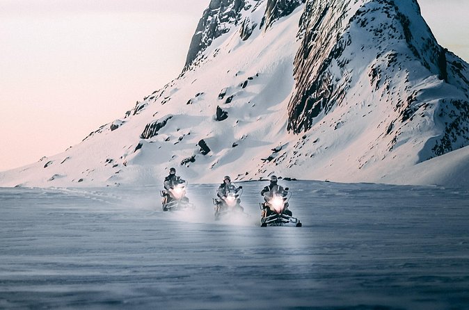 Snowmobile group riding below a snowy mountain on Langjökull