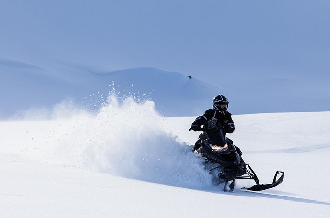 A helmeted rider on a snowmobile crossing a snowy landscape on the Glacier Rush tour