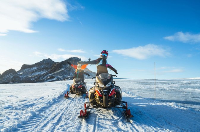 Two riders on a snowmobile with mountains behind them at Langjökull