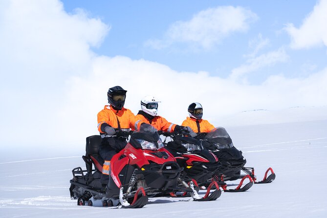 A driver and passenger on a shared snowmobile beside another rider on Langjökull